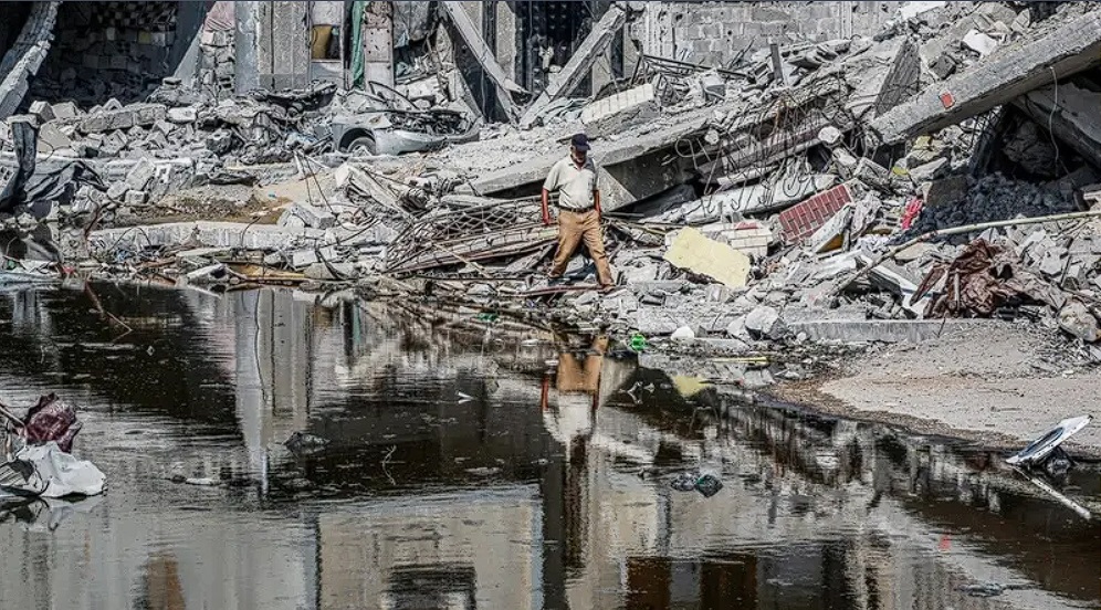 Ένας άνδρας περνά μπροστά από κατεστραμμένα κτίρια και μια λακκούβα με λύματα που ξεσπούν από κατέρρευσαν υπόγειους σωλήνες στο Χαν Γιούνις